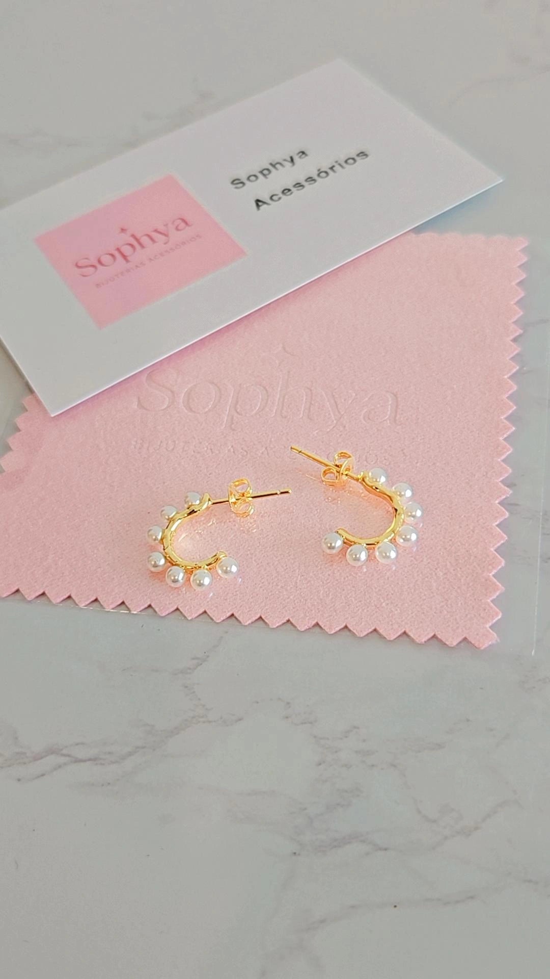 Estes são brincos de argola dourados com pérolas da marca Sophya Acessórios
