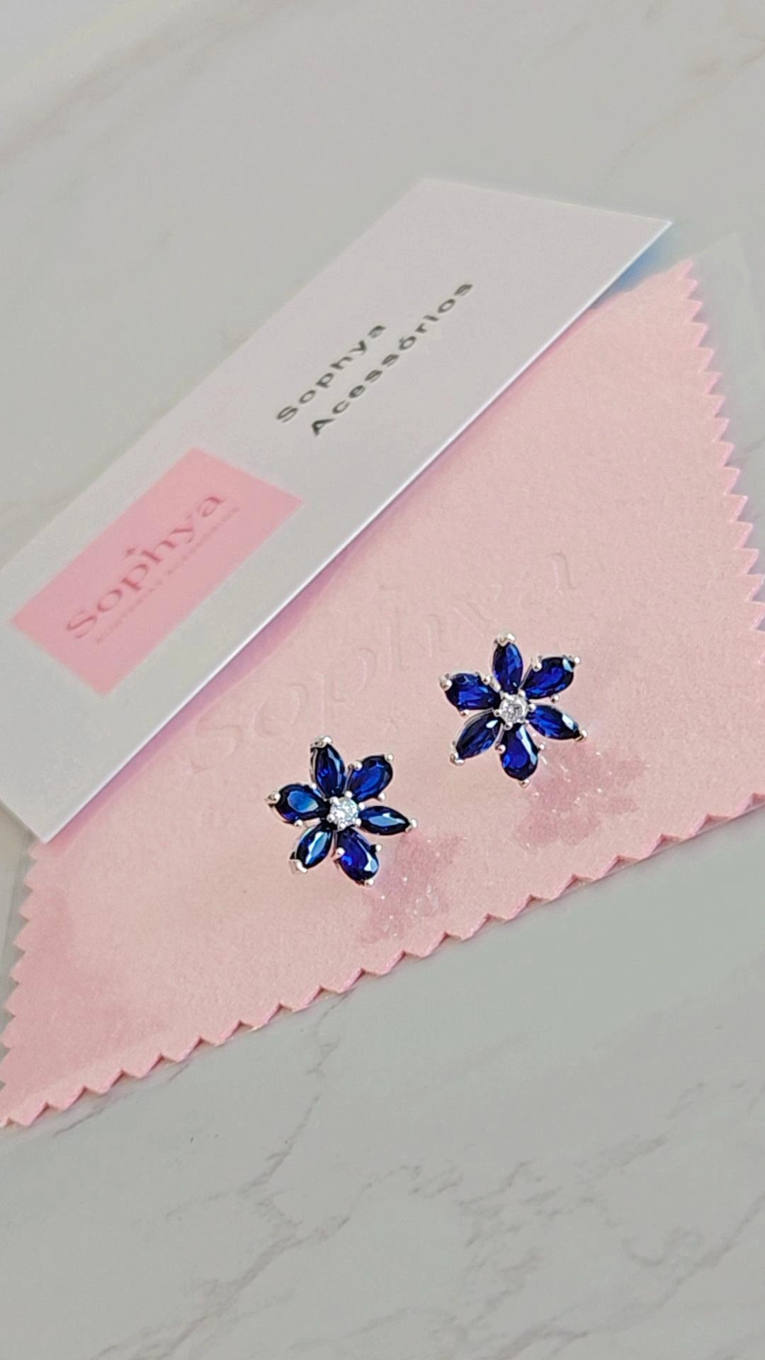 Estes são brincos de flores azuis da marca Sophya Acessórios.